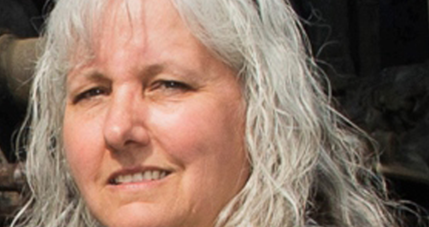 Middle-aged woman with long gray hair, smiling with a neutral background.